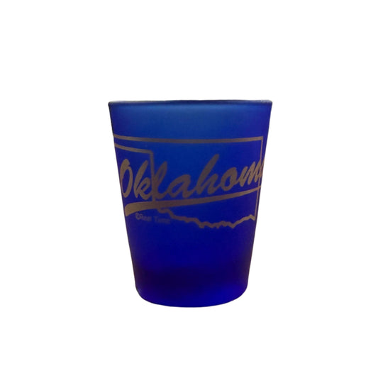 Cobalt blue shot glass with gold outline of Oklahoma and script text