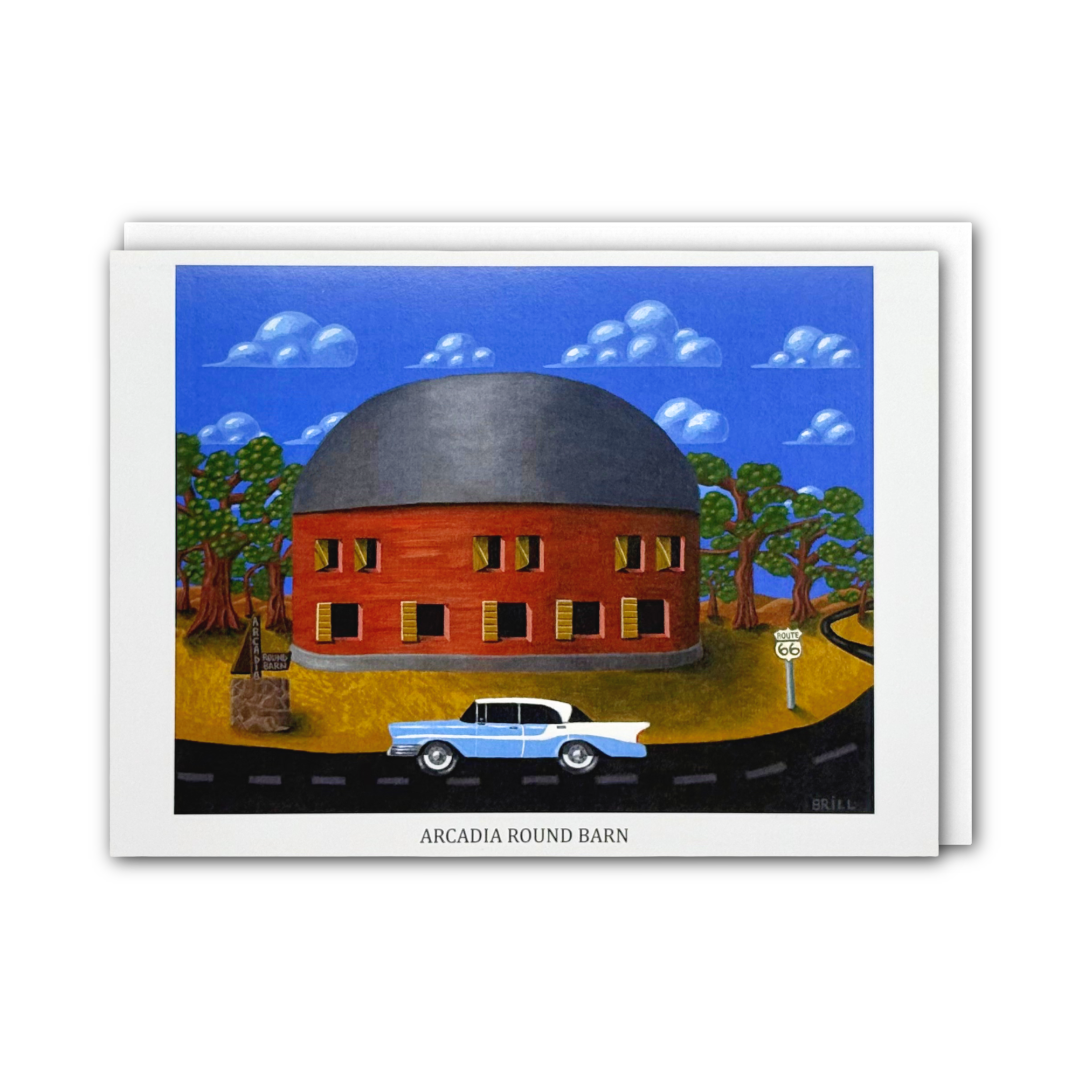 A printed art card showing a stylized red round barn with a dark gray dome, blue sky, clouds, trees, a road, and a light blue classic car. The card has a white border and the text 'ARCADIA ROUND BARN' at the bottom, photographed against a light gray background.