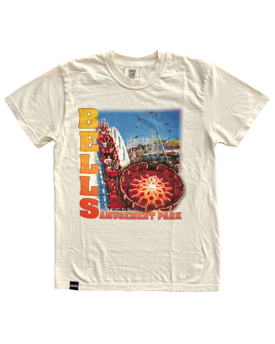 An off-white short-sleeve graphic t-shirt featuring a colorful print of Bells Amusement Park. The graphic includes the text 'BELL'S AMUSEMENT PARK' in red and yellow, depicting rides like a Ferris wheel, roller coaster, and a carousel.