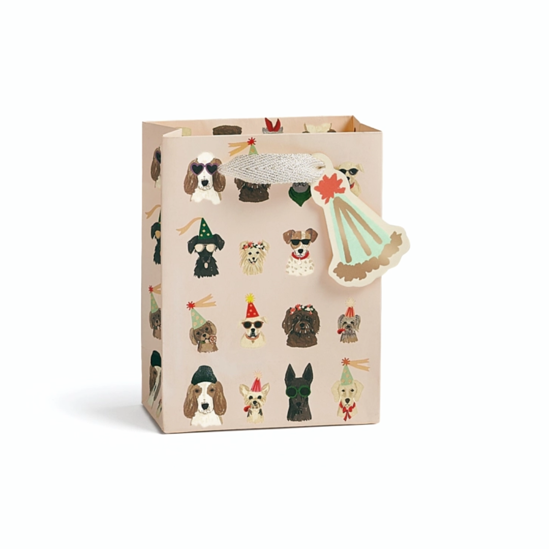 A beige gift bag decorated with illustrations of various dog breeds wearing party hats, featuring a white textured ribbon handle and a matching paper tag.