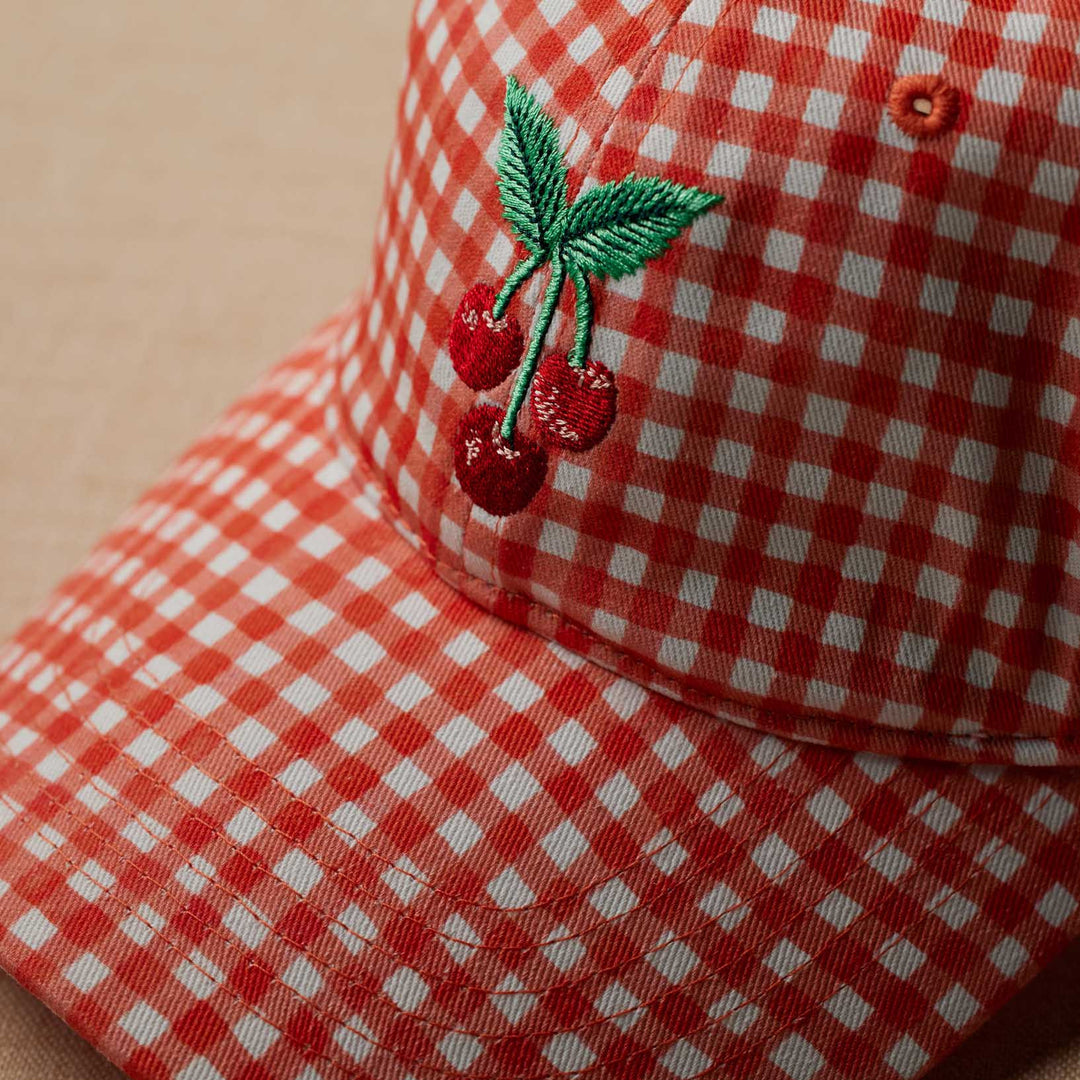 Red and white checkered cap with cherry design on a beige background