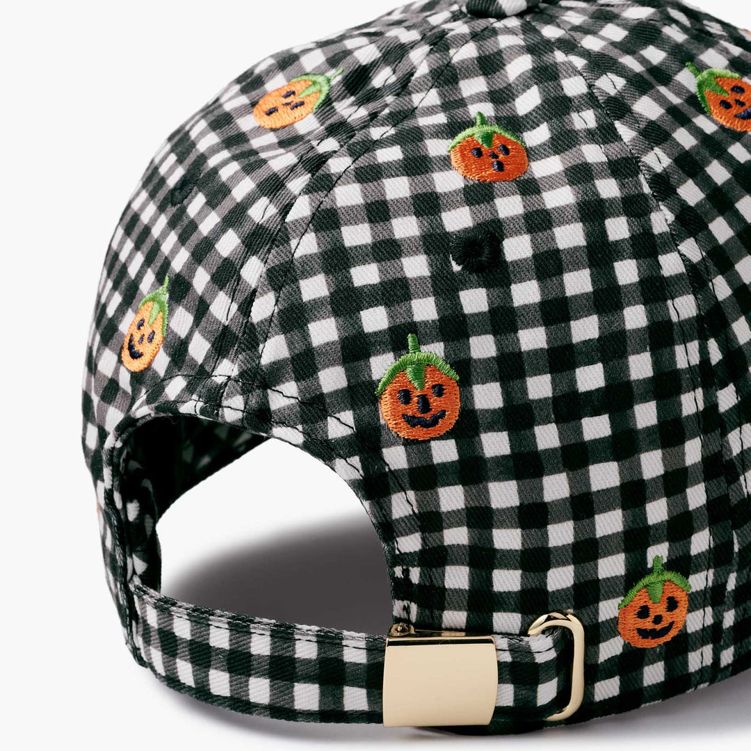 A close-up of a baseball cap featuring a black and white gingham pattern with embroidered orange pumpkin faces, shown on a light gray background.