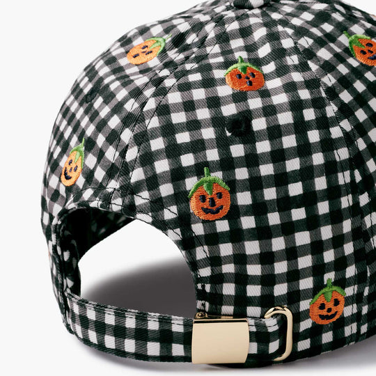 A close-up of a baseball cap featuring a black and white gingham pattern with embroidered orange pumpkin faces, shown on a light gray background.