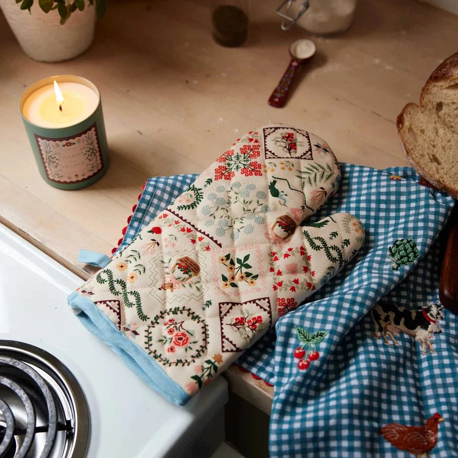 A rustic patterned oven mitt sits on a wooden surface with a lit candle.