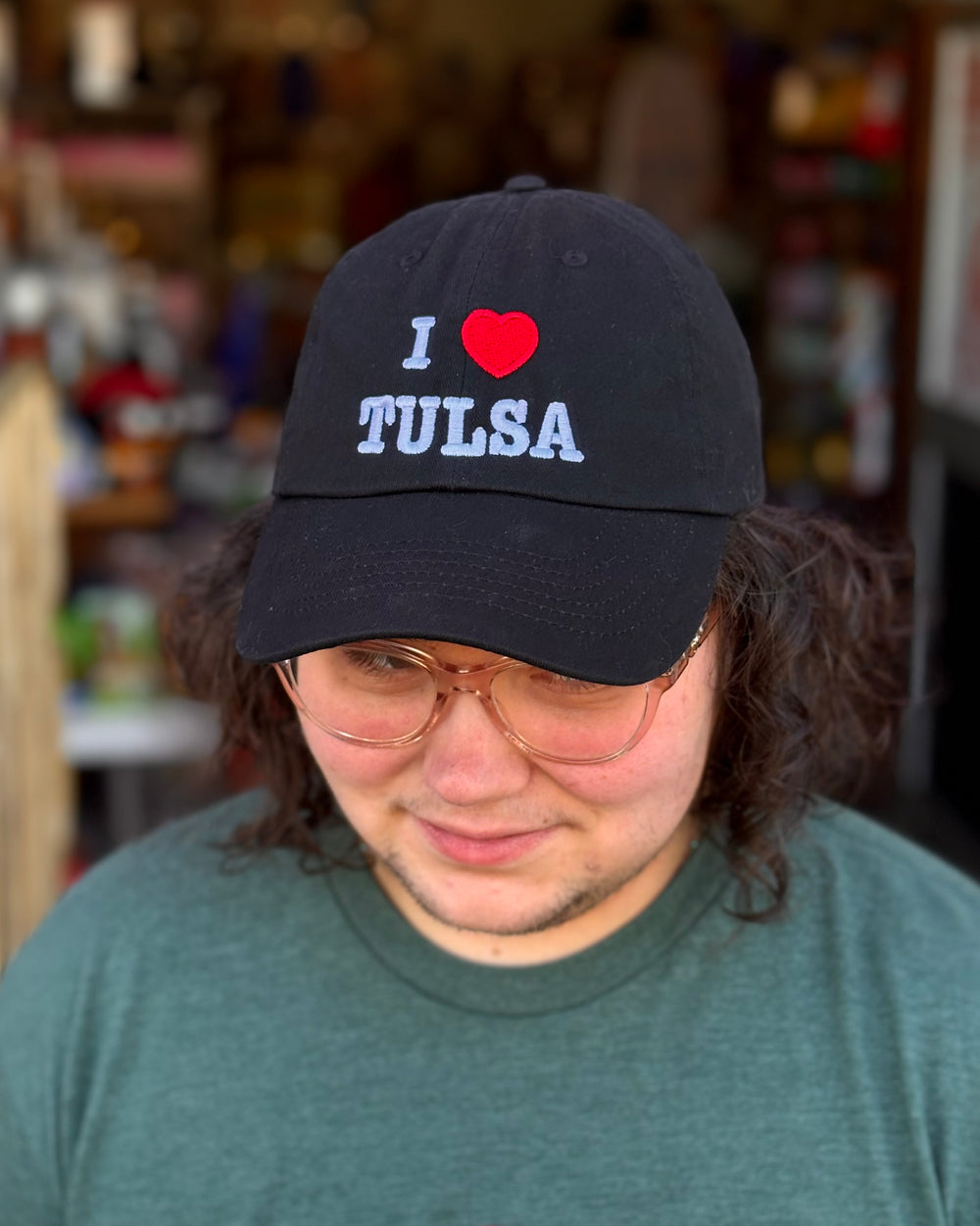A person smiles while wearing a black hat with the text "I ❤️ TULSA".
