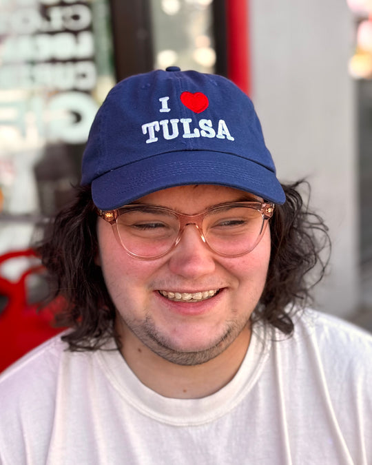 A person smiles while wearing a blue hat with the text "I ❤️ TULSA".