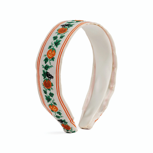 A white fabric headband featuring a Halloween-themed pattern of orange pumpkins, black crows, and green ivy leaves, bordered by thin orange stripes, shown on a plain white background.
