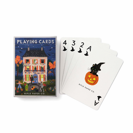 A boxed deck of playing cards with the front cover art showing a haunted house at night and the cards fanned out beside it. The visible card design includes black 4, 3, 2, and A cards with witch hats and a jack-o'-lantern with a black cat.