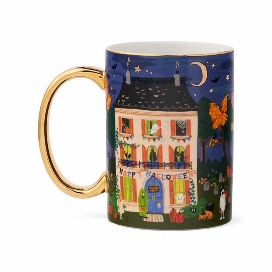 A ceramic mug with a gold handle and rim, featuring a colorful illustration of a haunted house at night for Halloween, set against a plain white background.