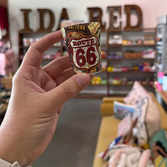 Shot glass featuring Route 66 shield and weathered travel posters from states along the historic route